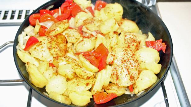 Gebratene Kartoffeln mit Paprika und Zwiebeln in einer schwarzen Pfanne.