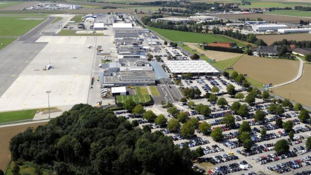 Luftaufnahme eines Flughafens mit Flugzeugen, Gebäuden und einem großen Parkplatz.