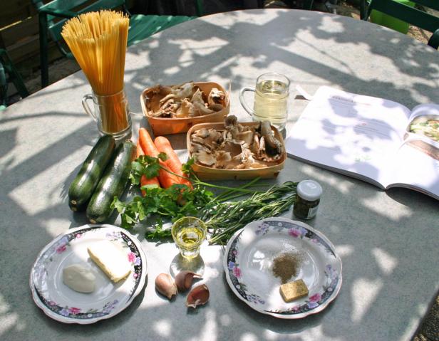 Zutaten für ein Nudelgericht mit Pilzen, Zucchini und Karotten auf einem Tisch angerichtet.