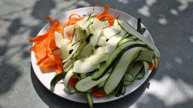 Ein Teller mit gehobelten Karotten und Zucchini liegt im Sonnenlicht.