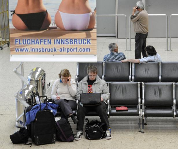 Wartende Reisende sitzen am Flughafen Innsbruck vor einer Werbetafel.