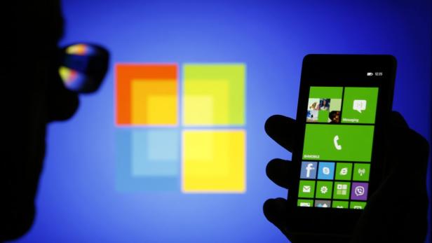 Eine Hand hält ein Smartphone mit Windows-Oberfläche vor einem Microsoft-Logo.