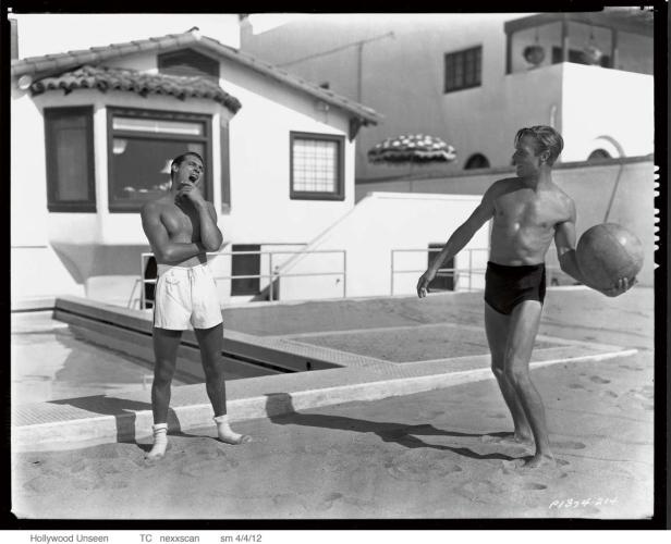 Zwei Männer in Badehosen posieren an einem Pool.