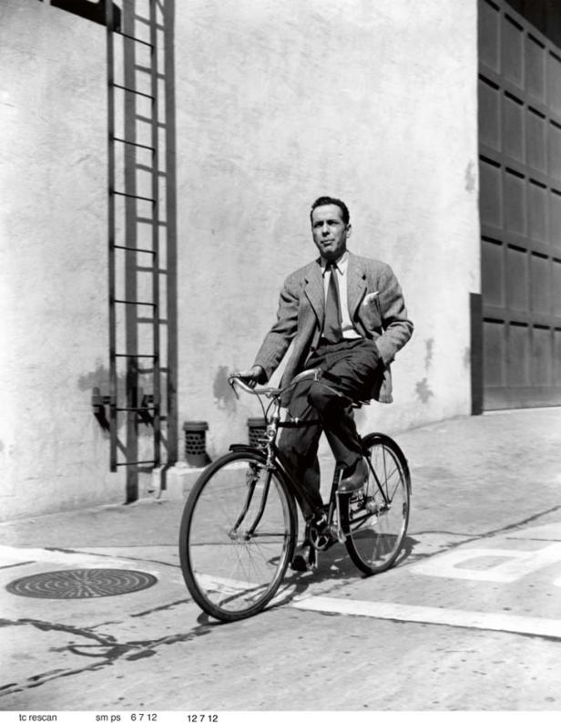 Humphrey Bogart fährt in einem Anzug Fahrrad.