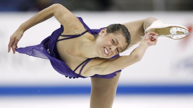Eine Eiskunstläuferin in einem lila Kleid führt eine Pirouette auf dem Eis aus.