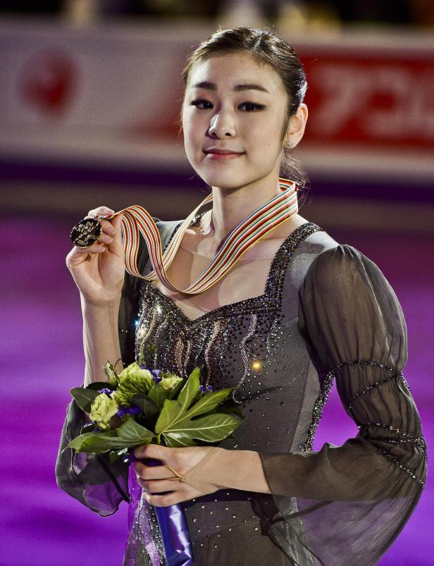 Eine Eiskunstläuferin mit Medaille und Blumenstrauß.