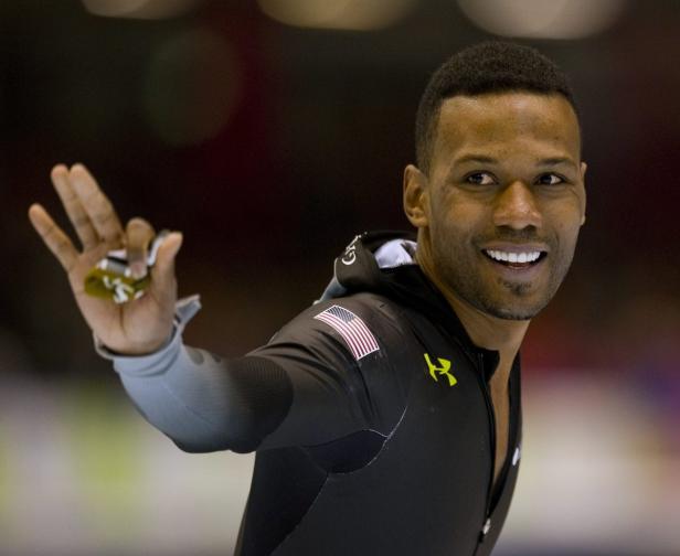 Shani Davis, ein US-amerikanischer Eisschnellläufer, lächelt und hält seine Handschuhe hoch.