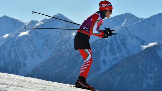 Eine Skifahrerin in roter Sportbekleidung fährt vor einer Bergkulisse Ski.