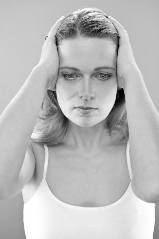 Eine Frau hält ihre Hände an ihren Kopf, möglicherweise aufgrund von Stress oder Kopfschmerzen.