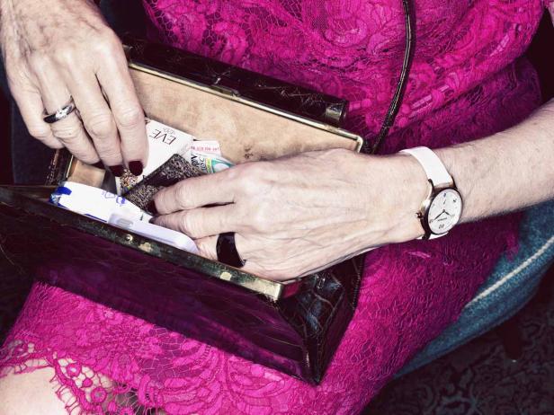 Eine Frau mit pinkfarbenem Kleid kramt in ihrer Handtasche.