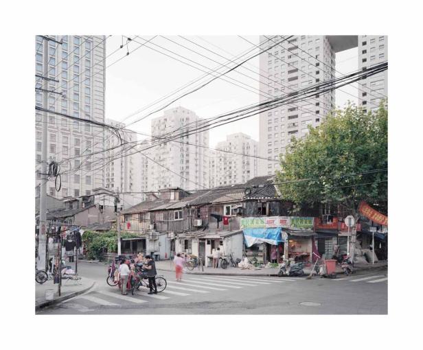 Eine Straßenszene in Shanghai mit alten Häusern und modernen Hochhäusern im Hintergrund.