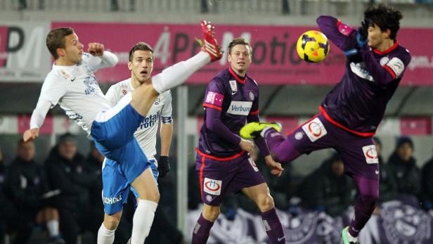 Ein Fußballspieler tritt nach dem Ball, während andere Spieler zusehen.
