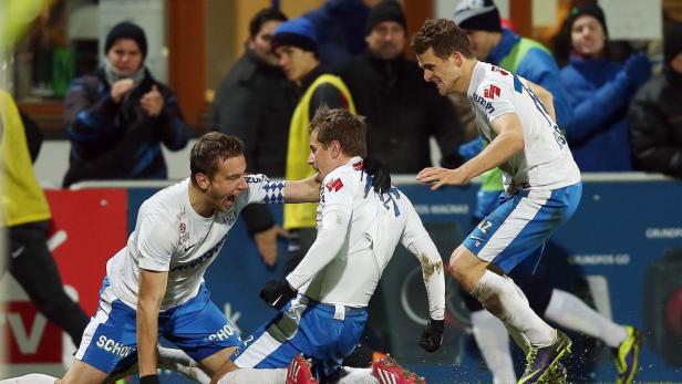 Drei Fußballspieler jubeln auf dem Spielfeld über einen Sieg.