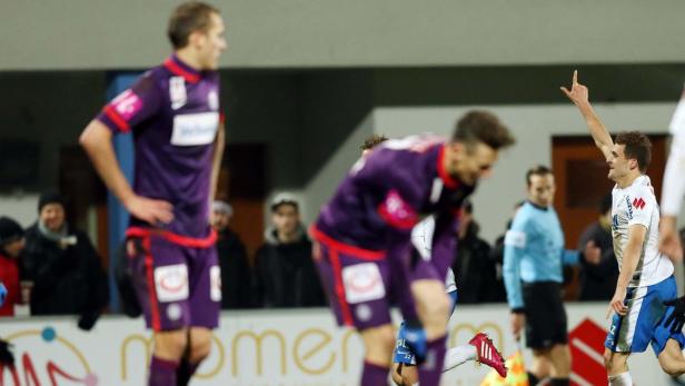 Ein Fußballspieler jubelt mit erhobenem Arm, während andere Spieler im Hintergrund stehen.