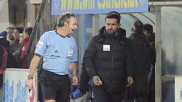 Ein Schiedsrichter und ein Trainer stehen am Spielfeldrand.