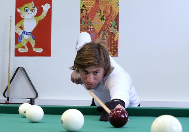 Ein Mann zielt mit einem Queue auf eine rote Billardkugel.