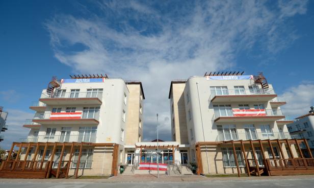 Das österreichische Haus mit Flaggen und „Austria“-Bannern unter blauem Himmel.
