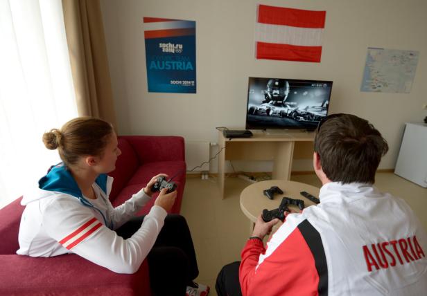 Zwei Personen spielen ein Rennspiel auf einer Konsole, im Hintergrund eine Österreich-Flagge.