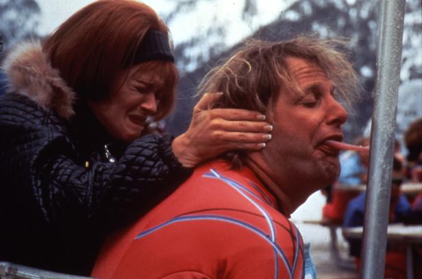 Eine weinende Frau hält den Kopf eines Mannes fest, der seine Zunge an eine Metallstange hält.