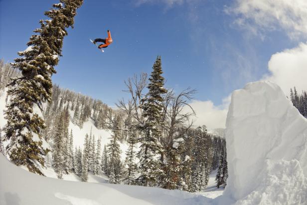 Ein Snowboarder springt vor einer verschneiten Berglandschaft in der Luft.