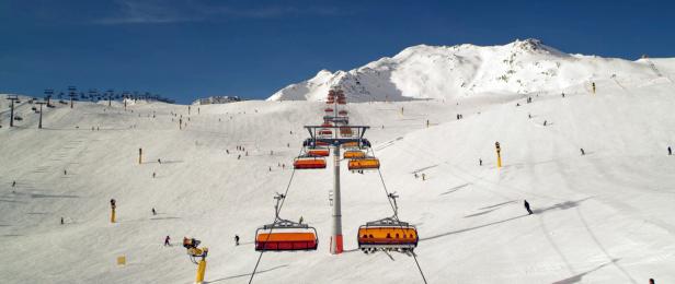 Eine orangefarbene Gondelbahn befördert Skifahrer einen schneebedeckten Berg hinauf.
