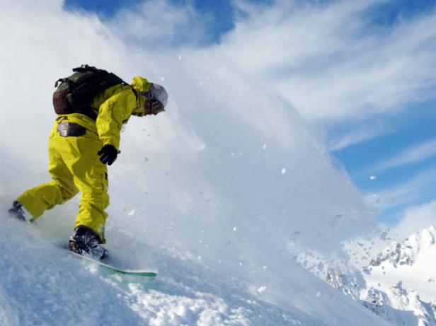 Ein Snowboarder in gelber Kleidung fährt einen schneebedeckten Hang hinunter.