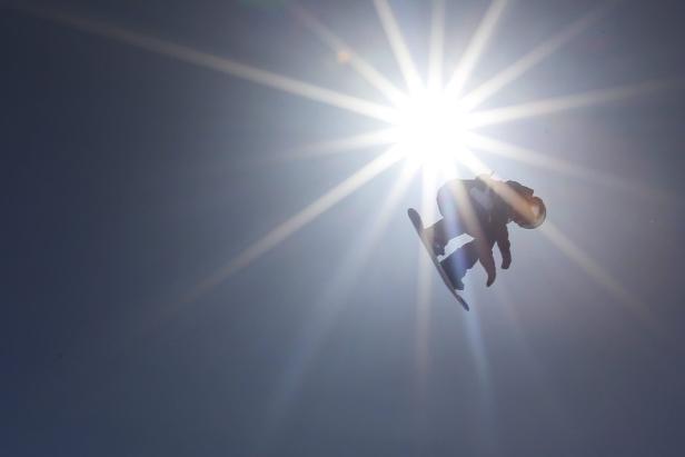 Ein Snowboarder springt vor der Sonne in der Luft.