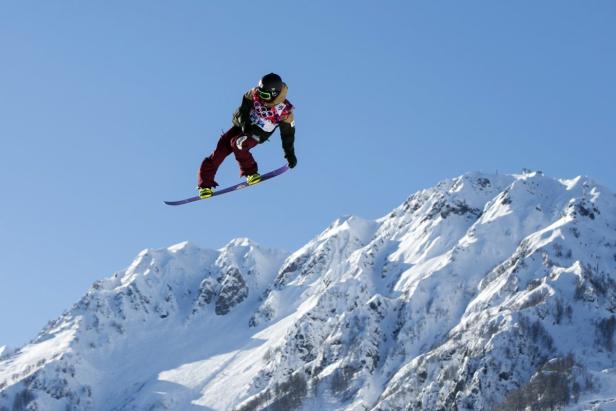 Ein Snowboarder springt vor einer verschneiten Bergkulisse.