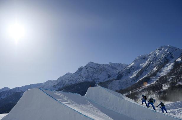 Drei Arbeiter präparieren eine Halfpipe vor einer verschneiten Bergkulisse.