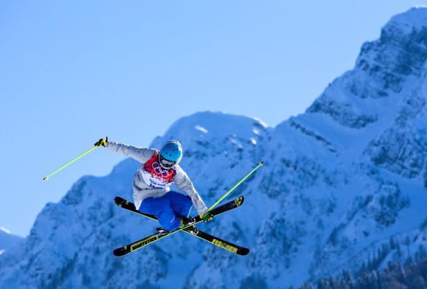 Ein Skifahrer springt vor einer verschneiten Bergkulisse in der Luft.