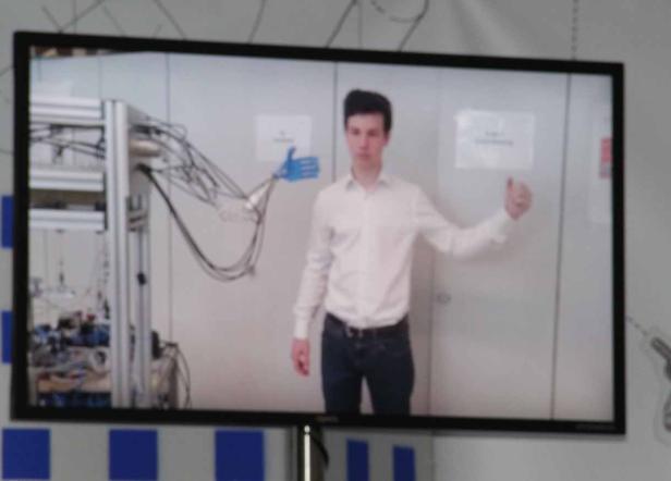 Ein junger Mann präsentiert eine Roboterhand auf einem Bildschirm.
