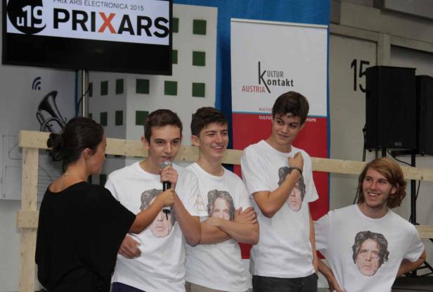 Eine Gruppe junger Leute mit T-Shirts mit einem Porträt vor einem „Prix Ars“-Hintergrund.