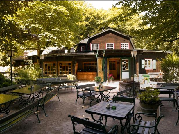 Ein Biergarten vor einem traditionellen Holzhaus im Grünen.