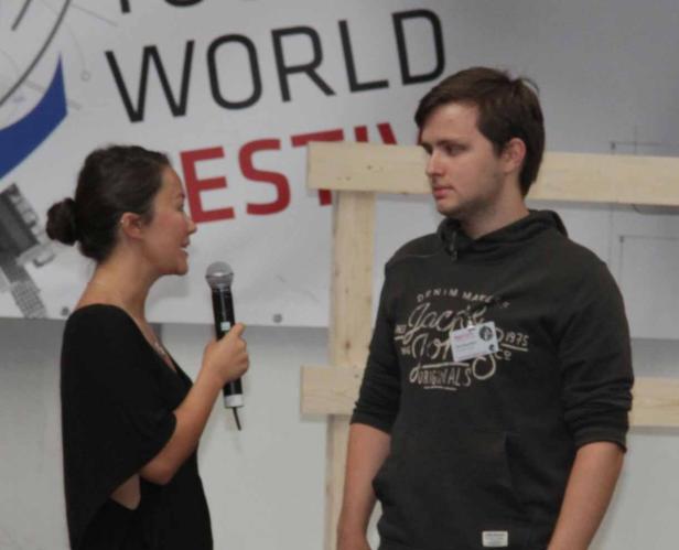 Eine Frau spricht mit einem Mikrofon zu einem Mann vor einem Banner.