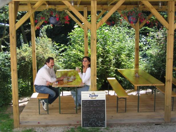 Ein Paar sitzt an einem Tisch in einem hölzernen Pavillon mit hängenden Blumenampeln.