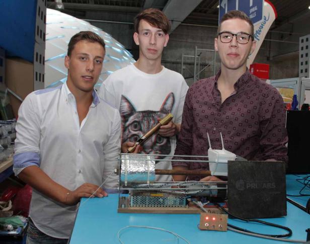 Drei junge Männer stehen an einem Stand mit technischer Ausrüstung.