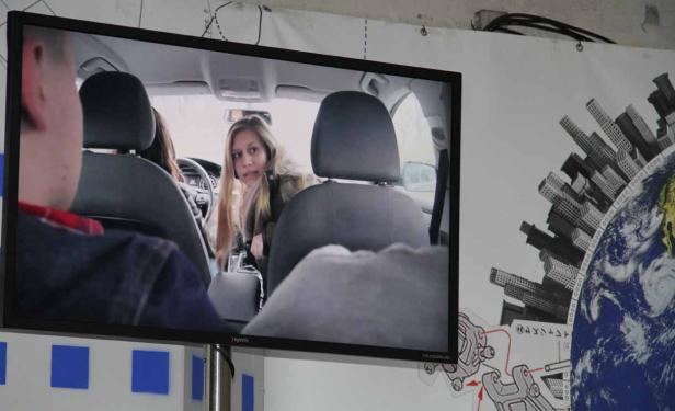 Ein Fernsehbild zeigt eine Frau, die auf dem Fahrersitz eines Autos sitzt.