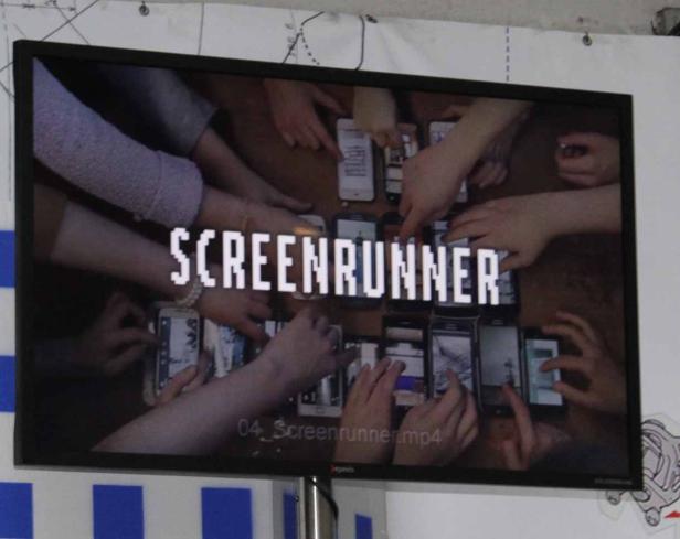 Ein Bildschirm zeigt das Wort „Screenrunner“ umgeben von vielen Händen und Smartphones.