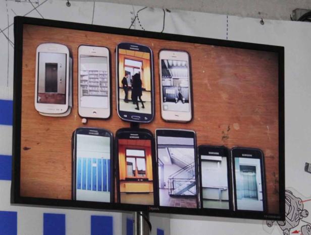 Ein Bildschirm zeigt eine Anordnung von Smartphones mit verschiedenen Gebäudeinnenräumen auf ihren Displays.