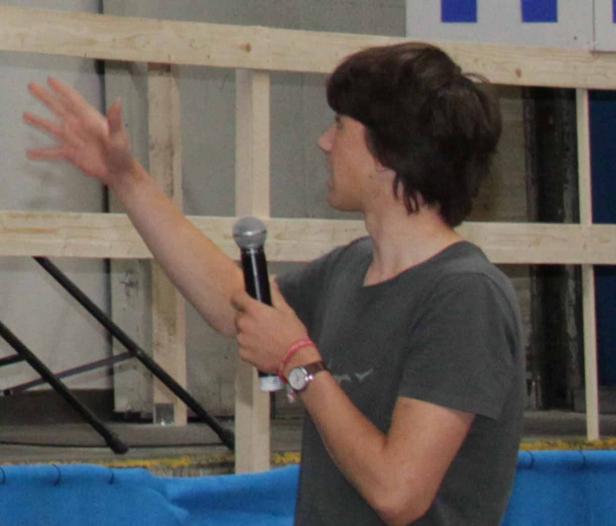 Ein junger Mann spricht in ein Mikrofon und gestikuliert mit der Hand.