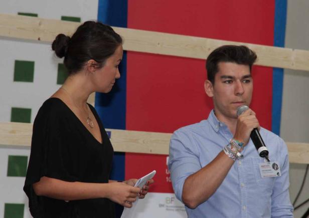 Ein Mann spricht in ein Mikrofon, während eine Frau neben ihm Notizen liest.