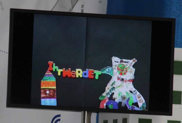 Auf dem Bildschirm ist eine Kinderzeichnung mit der Aufschrift „Ihr werdet“ zu sehen.