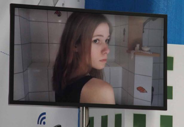 Ein Monitor zeigt das Bild einer jungen Frau vor einem Badezimmerhintergrund.