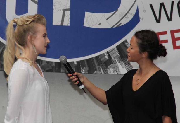 Eine Frau interviewt eine andere Frau mit einem Mikrofon vor einem Banner.