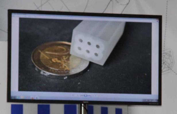 Auf dem Bildschirm ist ein Würfel mit Löchern neben einer Zwei-Euro-Münze zu sehen.