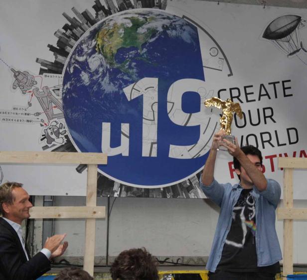 Ein junger Mann hält eine goldene Statue vor einem „Create Your World Festival“-Banner hoch.