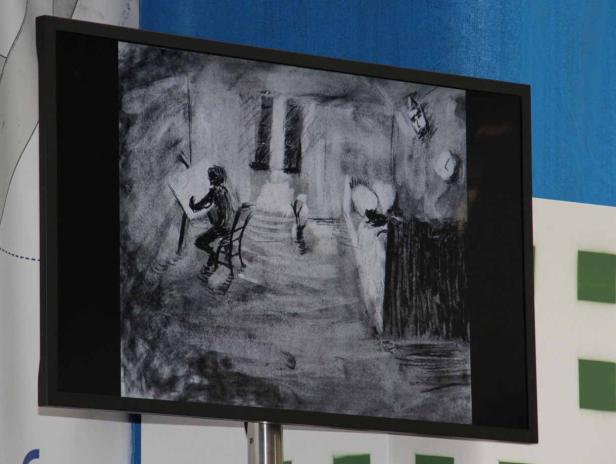 Ein Bildschirm zeigt eine Kohlezeichnung eines Künstlers bei der Arbeit.