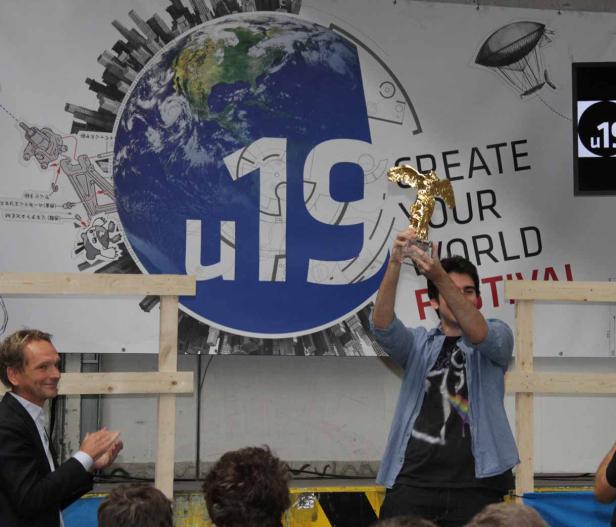 Ein Mann hält eine goldene Trophäe vor dem Hintergrund des „Create Your World“-Festivals hoch.