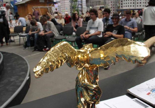 Eine goldene Statue mit Flügeln steht vor einer Gruppe von Menschen.