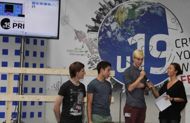 Eine Gruppe von Personen steht vor einem Poster für den „Prix Ars Electronica 19“.